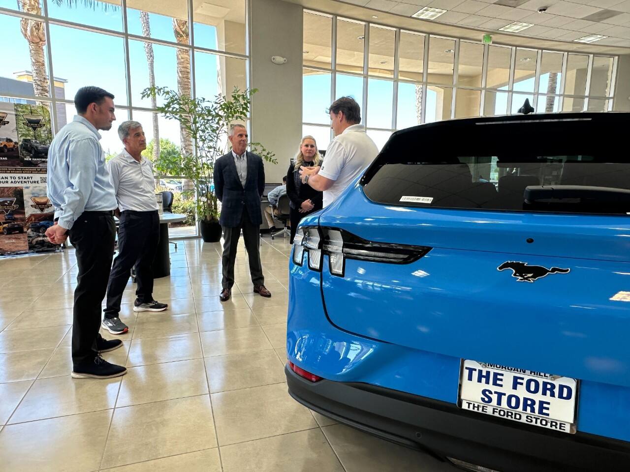 A group of people in formal attire speak in a car dealership show room.